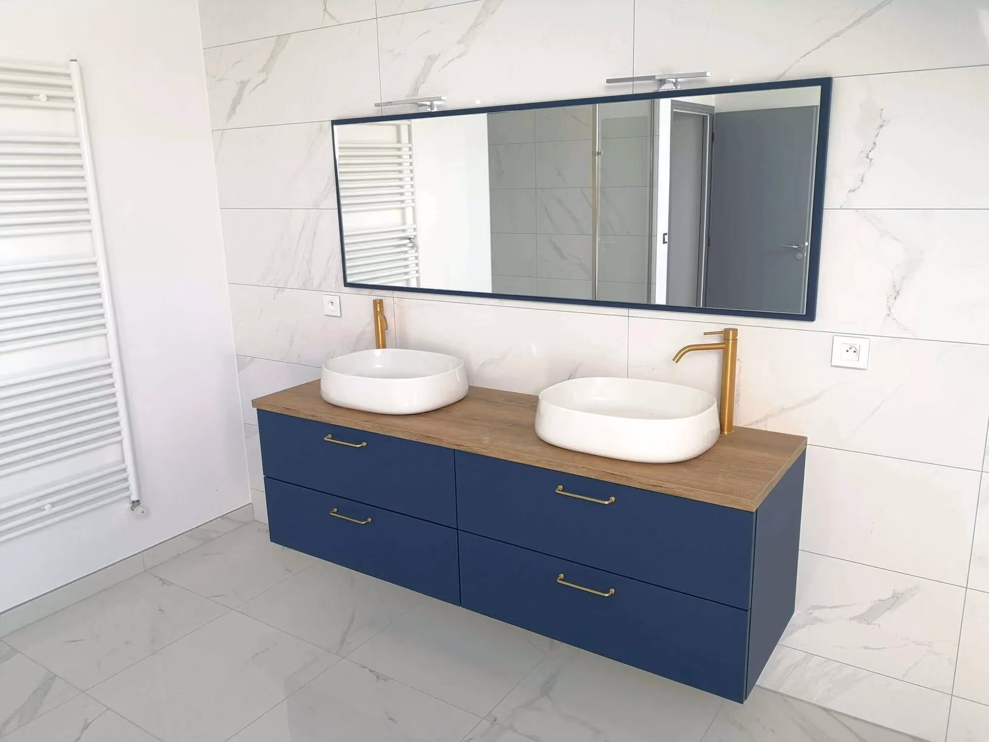 Meuble suspendu bleu à quatre tiroirs, deux vasques blanches à poser et robinets dorés sous un grand miroir