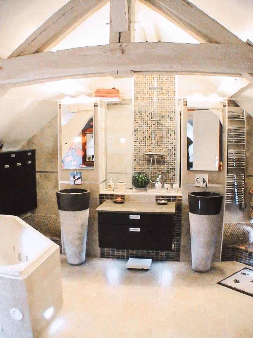 Salle de bains sous poutres avec meuble central sombre, vasques et baignoire
