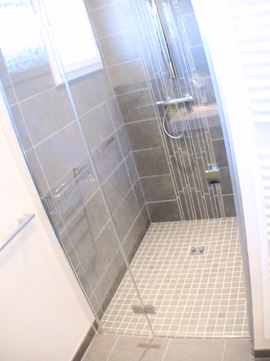 Douche étroite carrelée de gris avec paroi vitrée